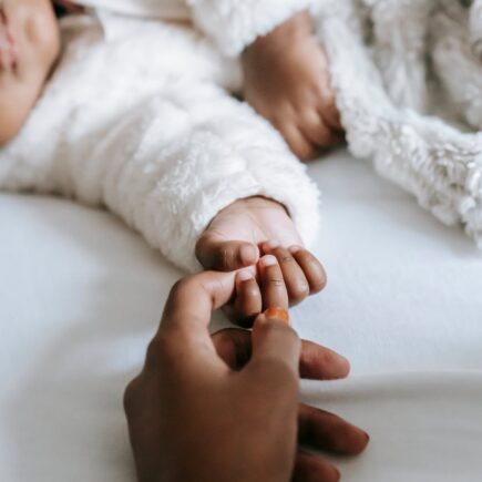 Mom holding baby's hand trying to bond.