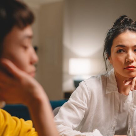 Two moms sitting together. One is judgingly looking at the other. Mom shaming takes many forms.