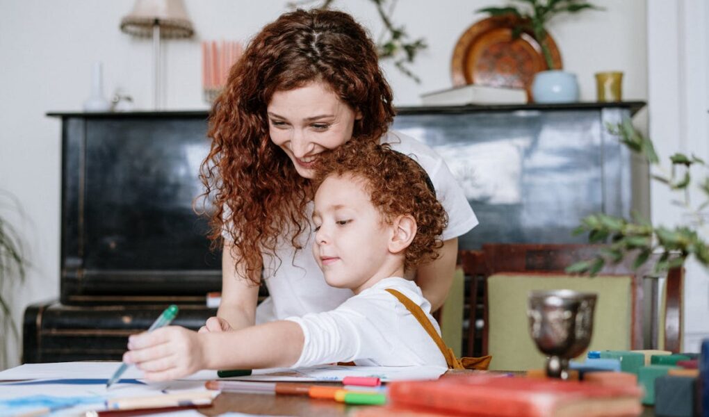 Mom sitting at the table spending time with her son as he draws.