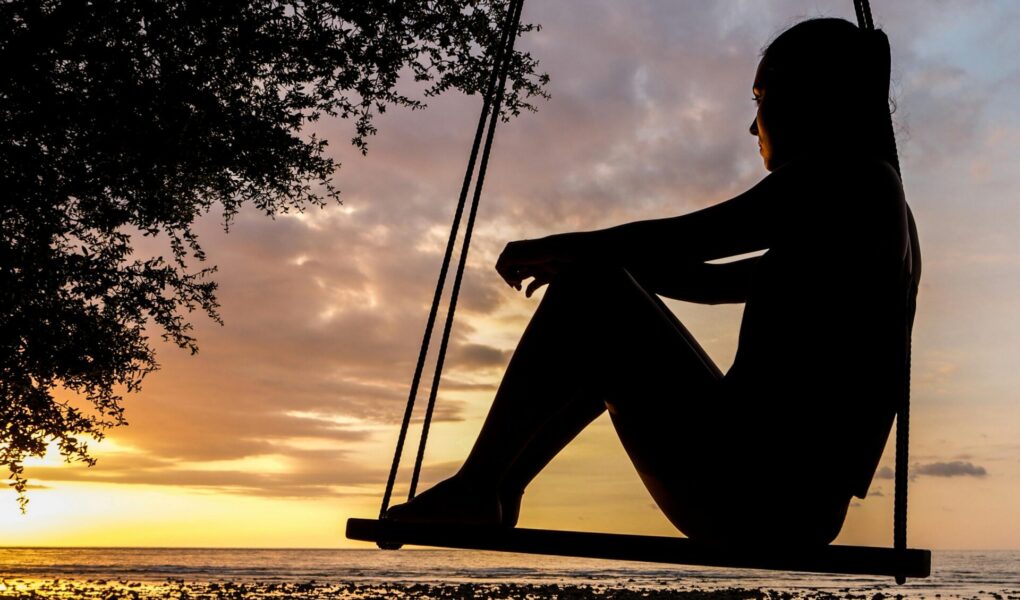 A woman sitting on a swing looking at the sunset and deep in thought.