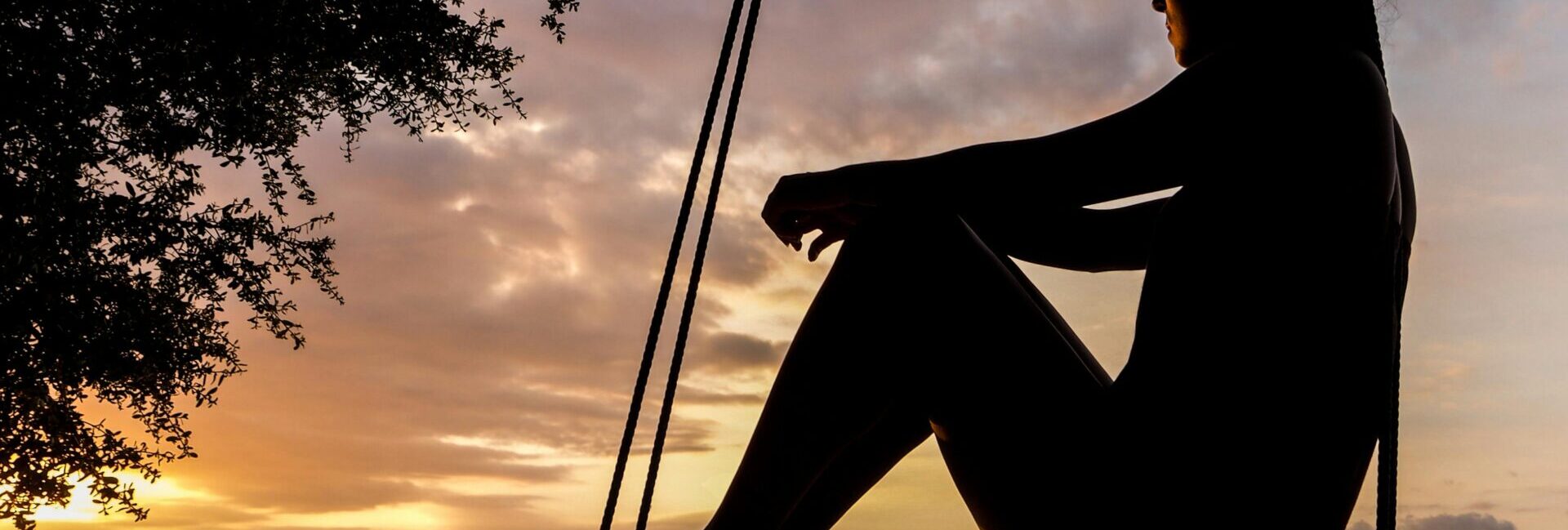 A woman sitting on a swing looking at the sunset and deep in thought.