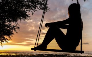 A woman sitting on a swing looking at the sunset and deep in thought.