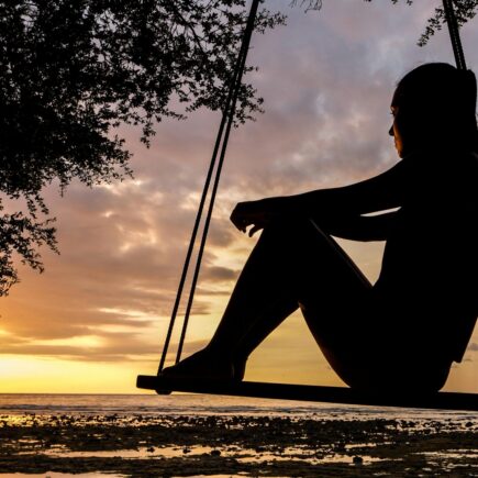 A woman sitting on a swing looking at the sunset and deep in thought.