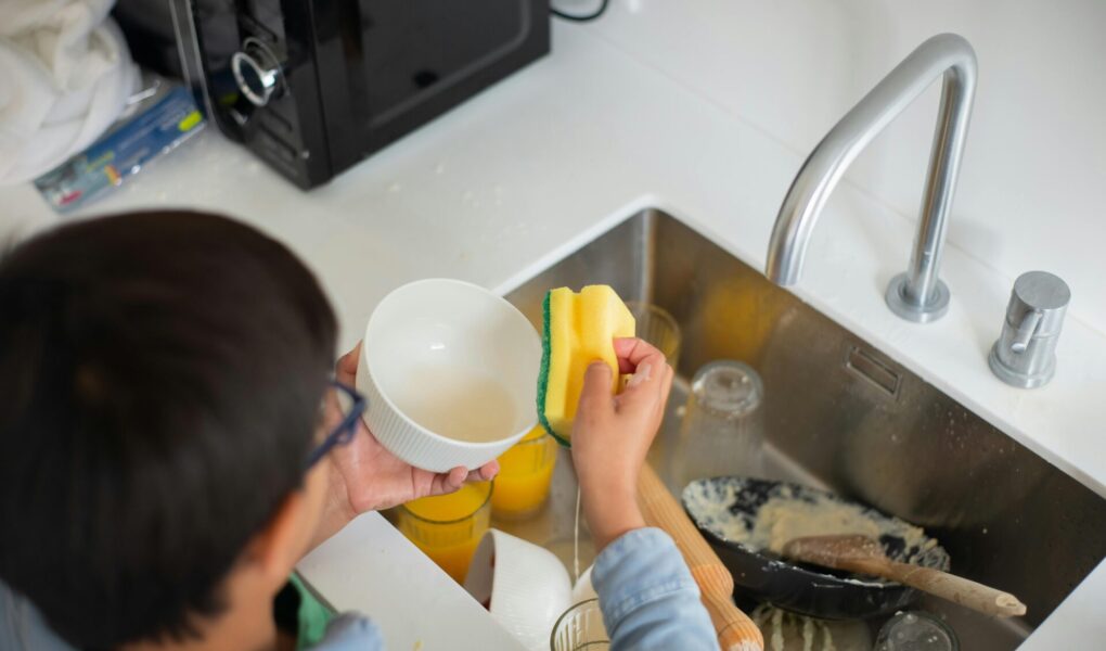 Boy cleaning dishes as part of his household chores.