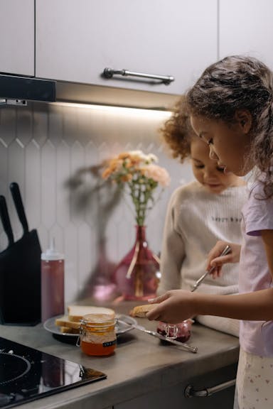 Young girl making a jelly sandwich while little brother is sitting next to her.