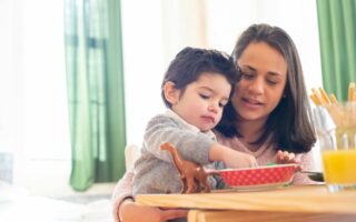 Mom sitting down with her son while he plays with his toys.