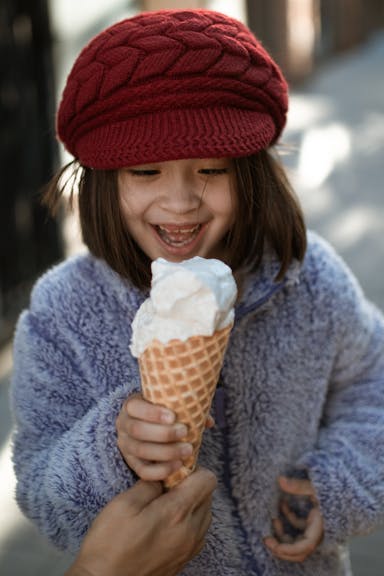 A child is being handed an ice cream cone. She is smiling and taking a hold of it to dig in.