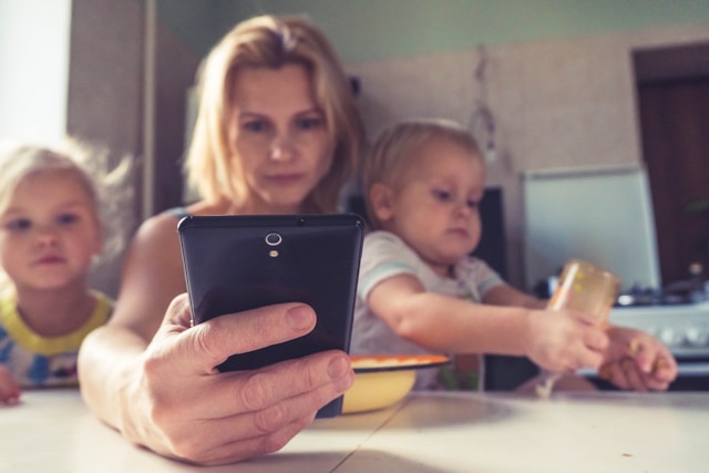 Mom looking at her phone while sitting at the table with her two children.
