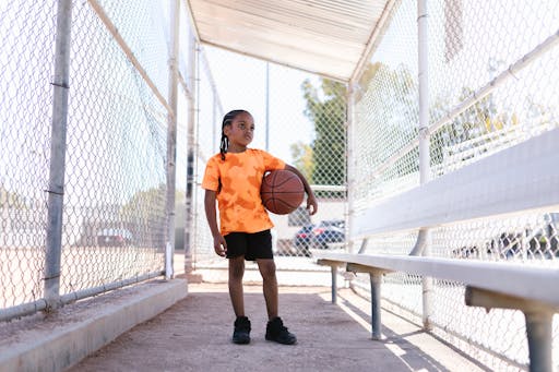 Boy standing in a dugout holding a basketball.