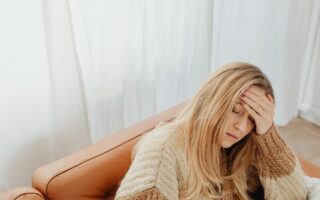 Woman sitting on the couch holding her head with one hand