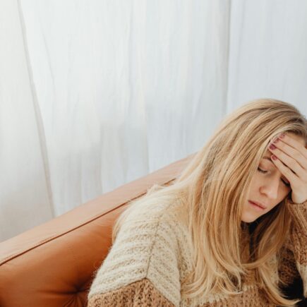 Woman sitting on the couch holding her head with one hand