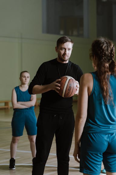 Parent coaching another person on basketball while his daughter watches from behind.