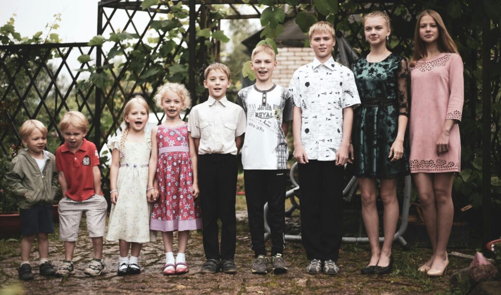 9 siblings standing in a row from youngest to oldest.
