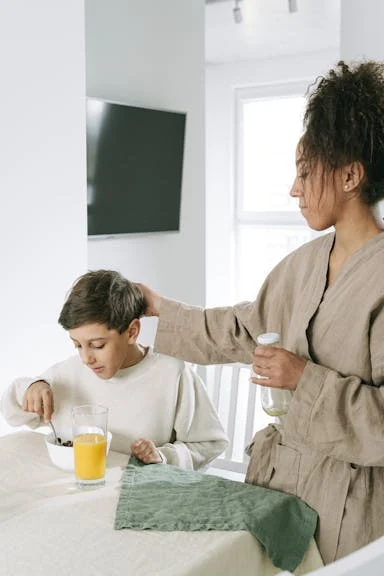 Mom has her hand on her son's head while he eats breakfast. The image signifies how a parent protects their child.