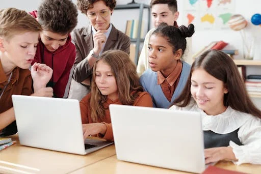 A group of preteens huddled together while looking at two laptops. The image shows that everyone wants to belong and be a part of a group.