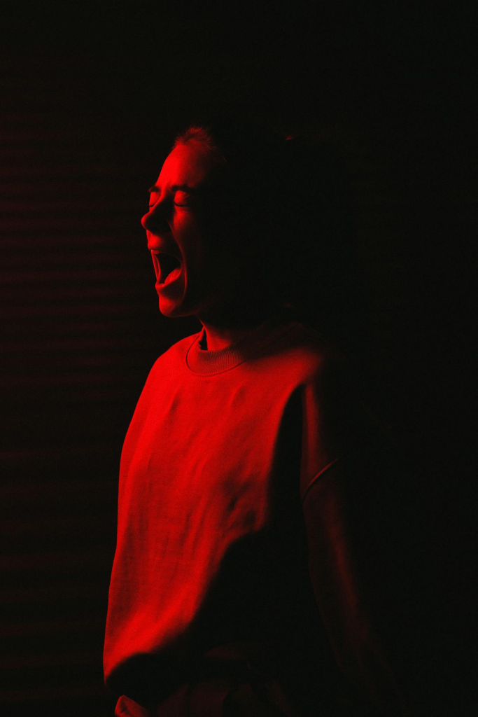 A woman yelling in the darkness with red light illuminating her face.